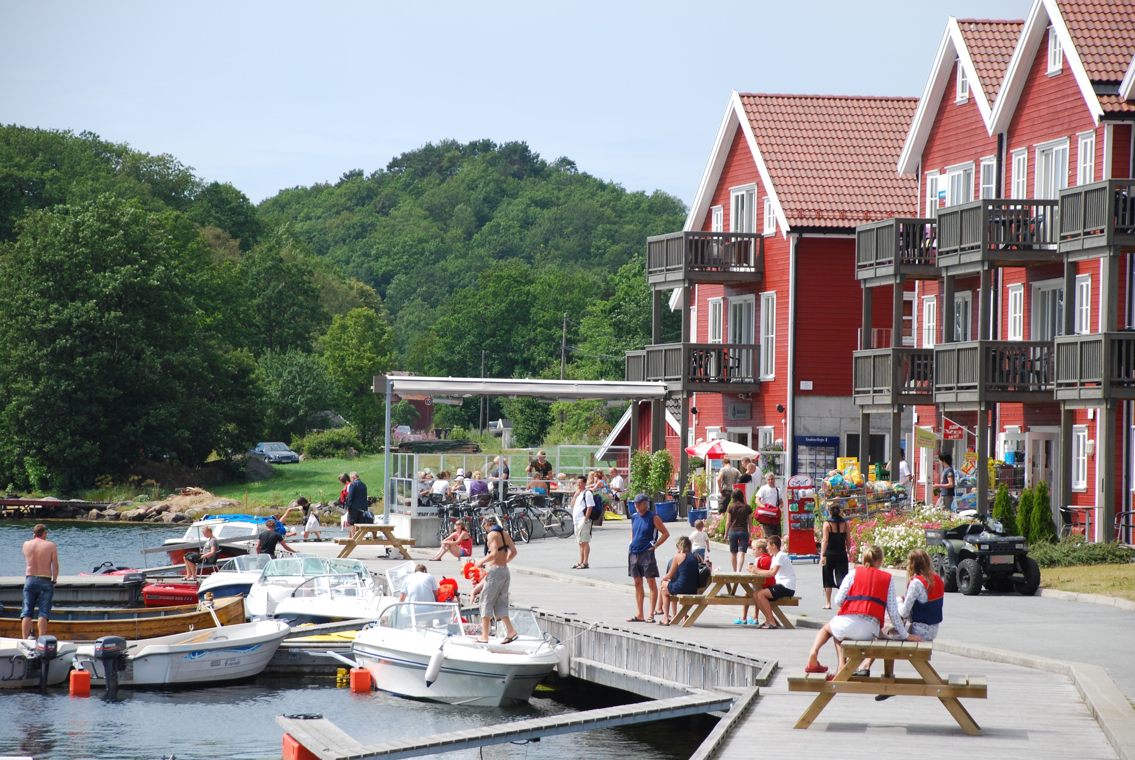 Mange mennesker på brygga ved den røde tregde feriehus på en solfylt dag