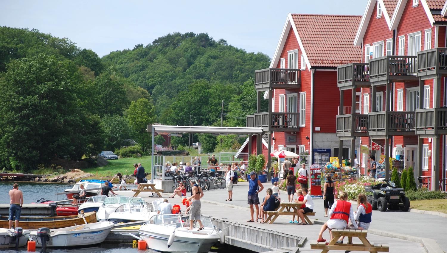 Mange mennesker på brygga ved den røde tregde feriehus på en solfylt dag