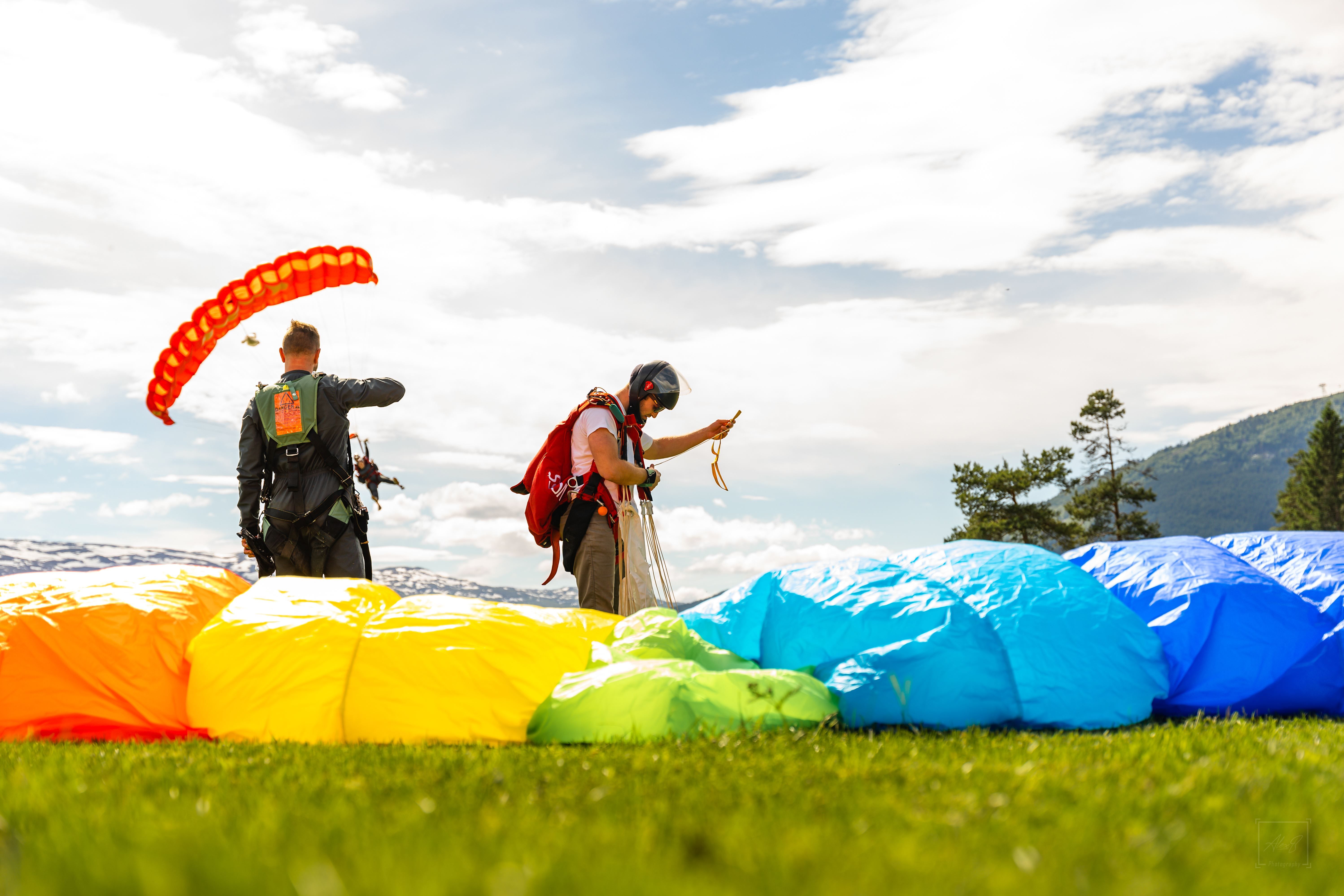 People on the ground right after landing a parachute. Multi‑coloured canopy on the ground near the camera. 