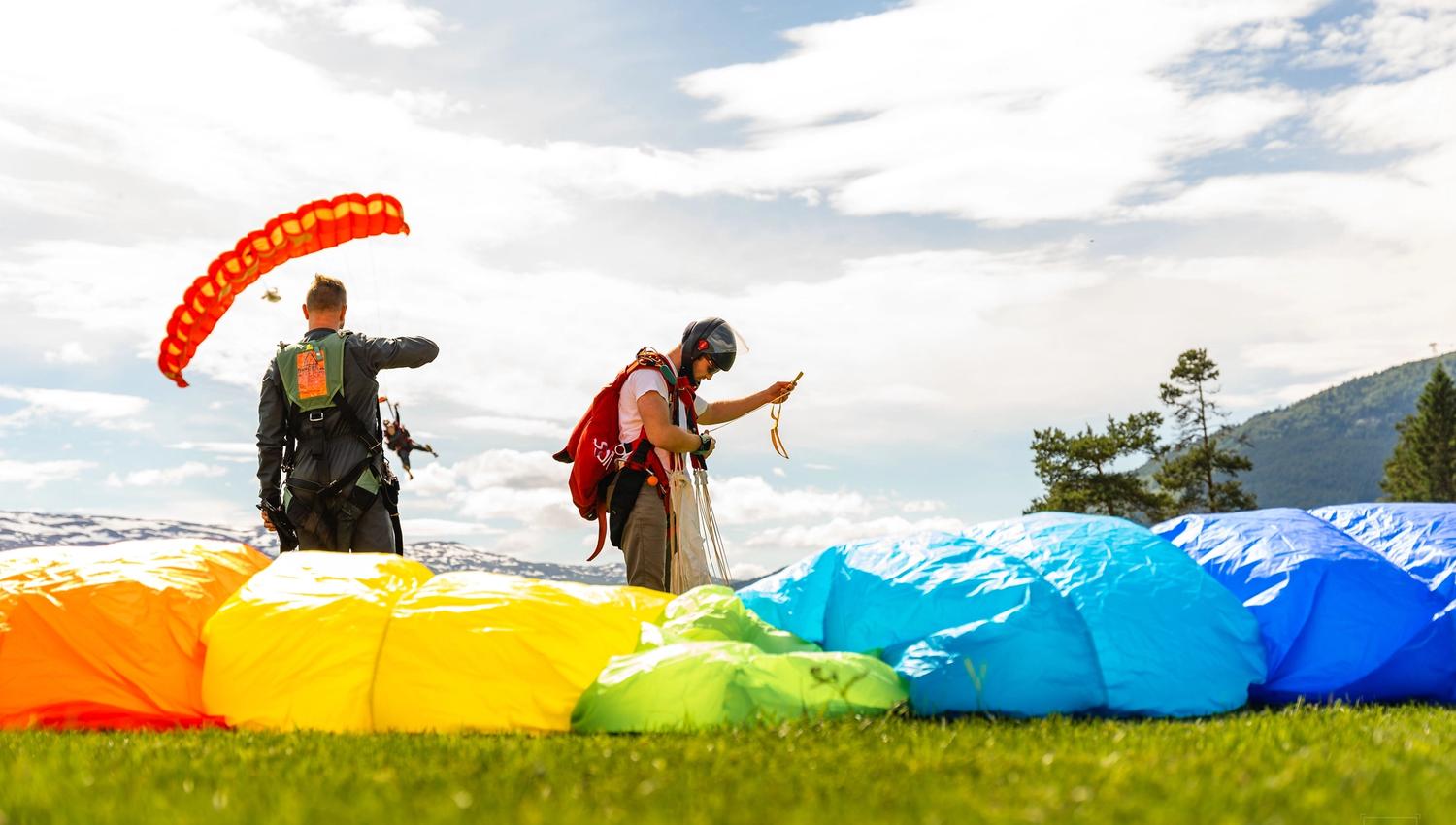 People on the ground right after landing a parachute. Multi‑coloured canopy on the ground near the camera.