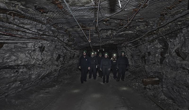 A group of guests with head lamps and helmets on, walking through a mine passage on a guided tour