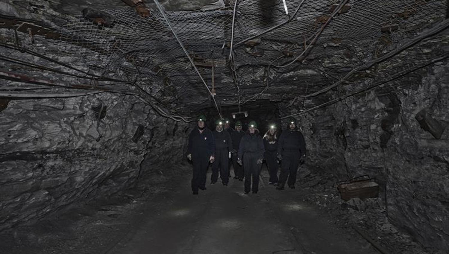 A group of guests with head lamps and helmets on, walking through a mine passage on a guided tour