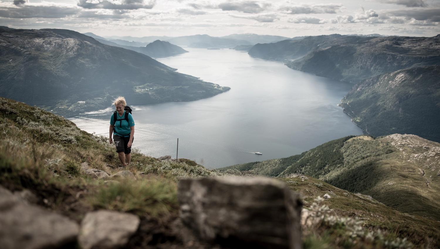 Ein turgåar stig oppover fjellsida med Hardangerfjorden i bakgrunnen.
