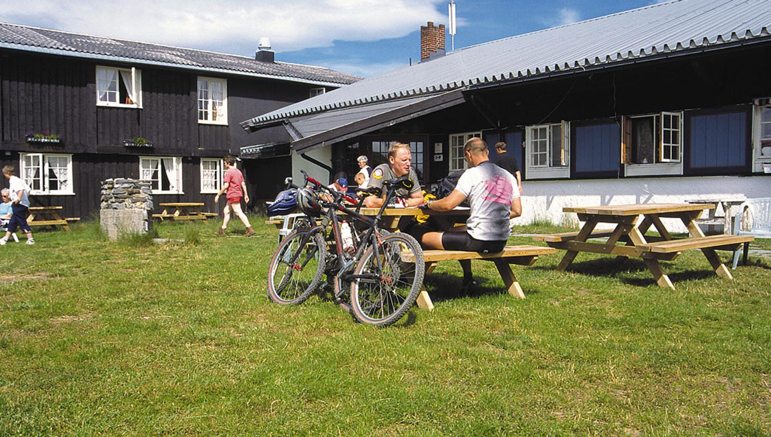 Cyclists enjoy a bite to eat at picknick tables on the lawn of a mountain lodge