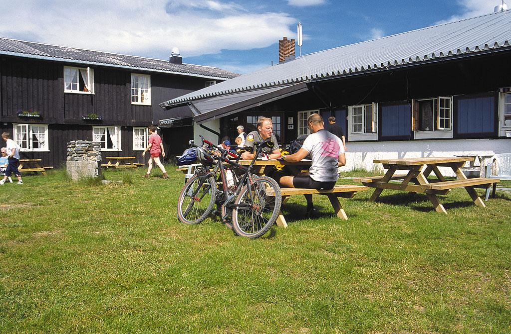 Cyclists enjoy a bite to eat at picknick tables on the lawn of a mountain lodge