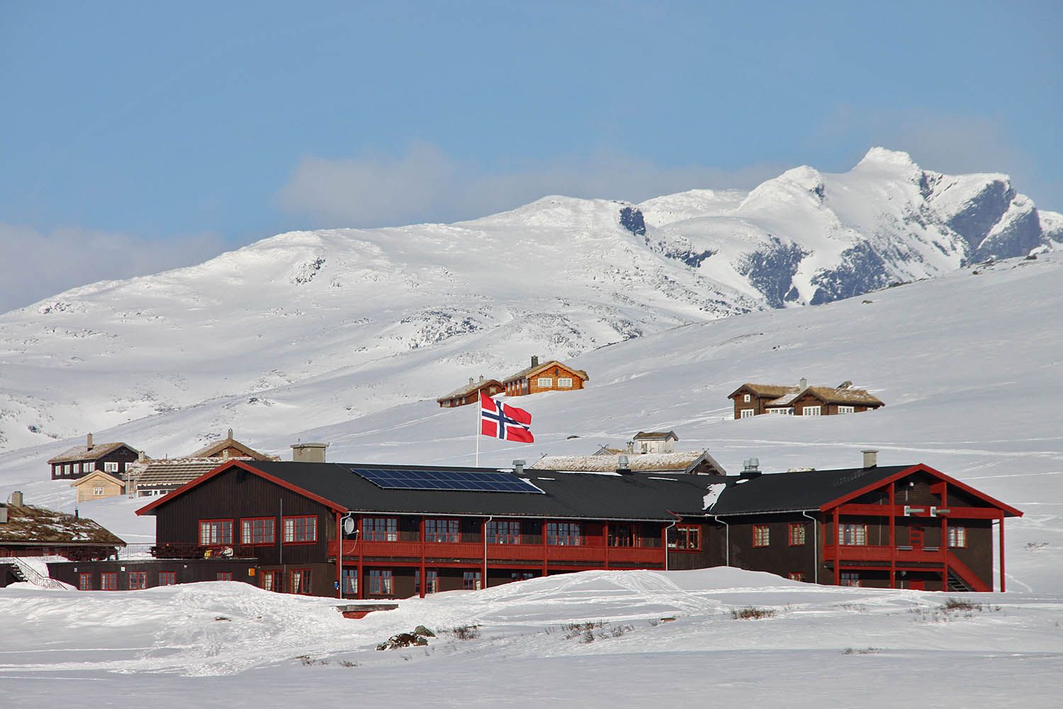 En fjellstue og et knippe hytter i et nedsnødd høyfjellslandskap