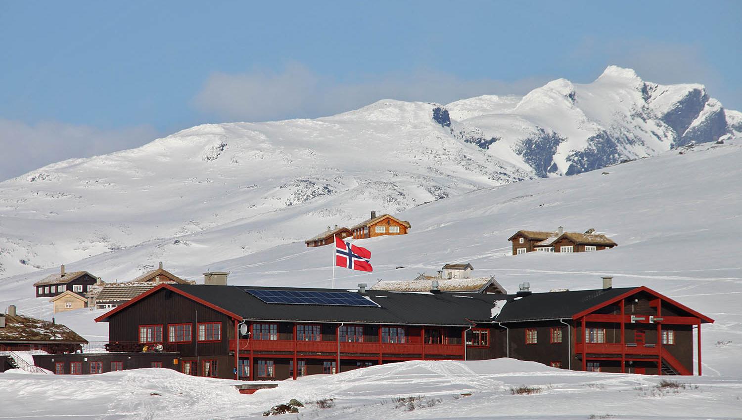 En fjellstue og et knippe hytter i et nedsnødd høyfjellslandskap