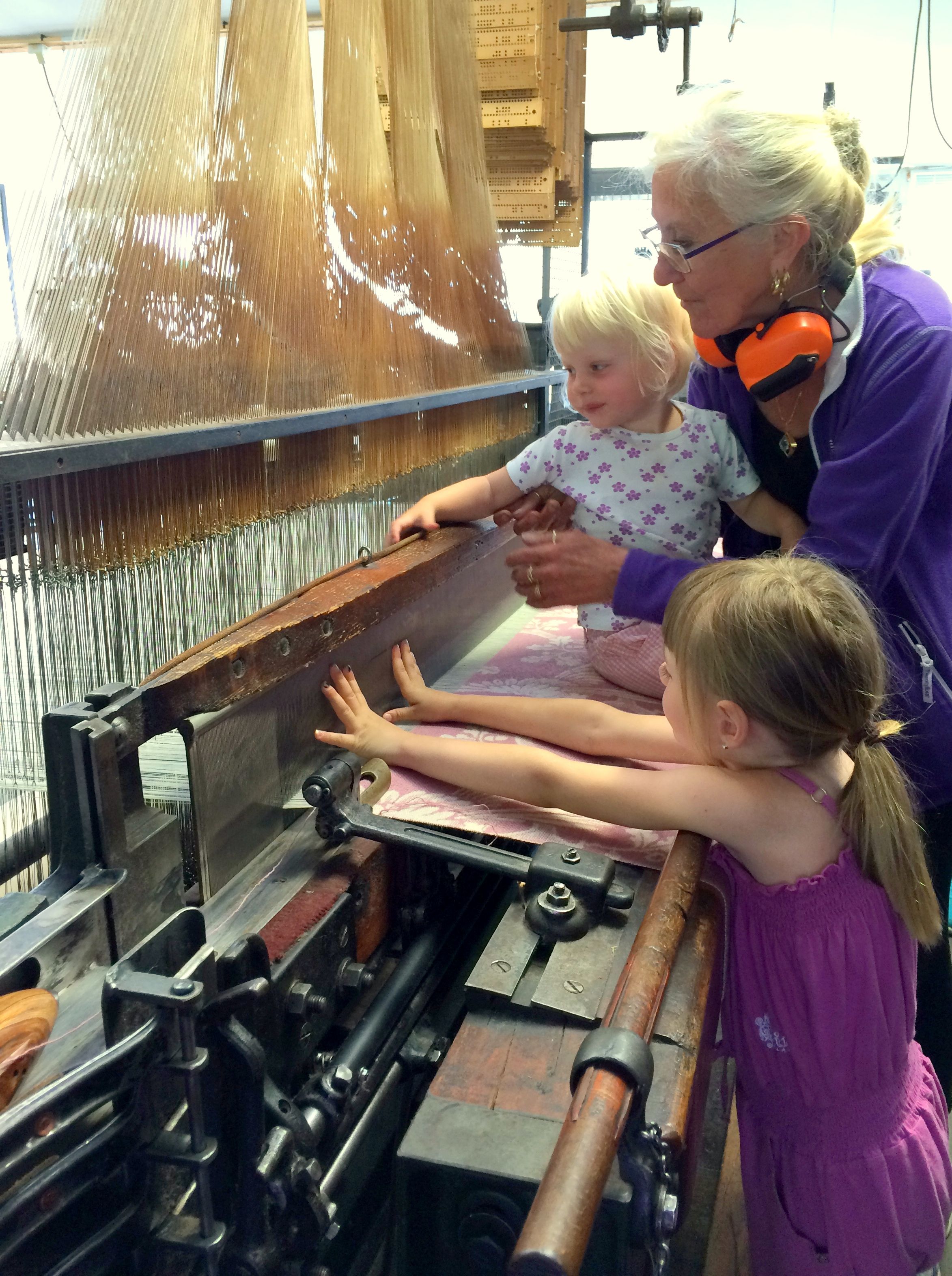 Two children and an adult feeling and touching the weaving machine.