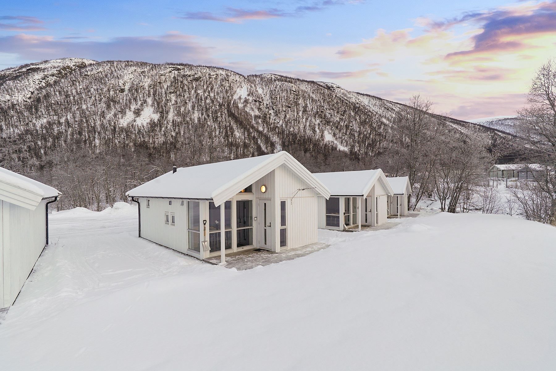 Three white houses in a snowy landscape with mountains and colourful sky in the background