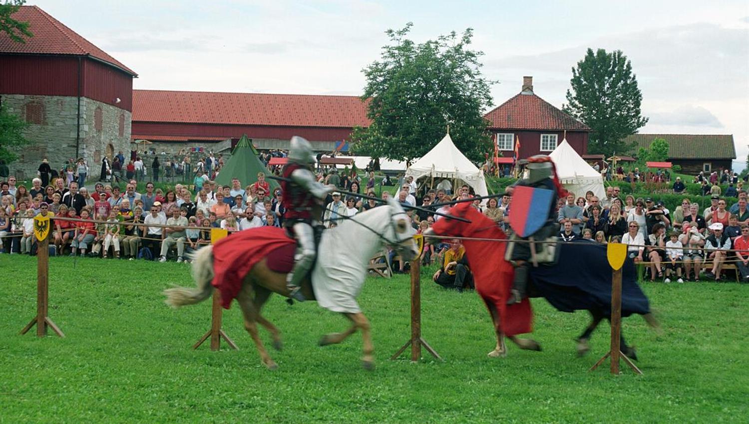 Outdoor area at Domkirkeodden, with children playing on the grassy lawn surrounded by traditional buildings. A lively and colourful atmosphere.