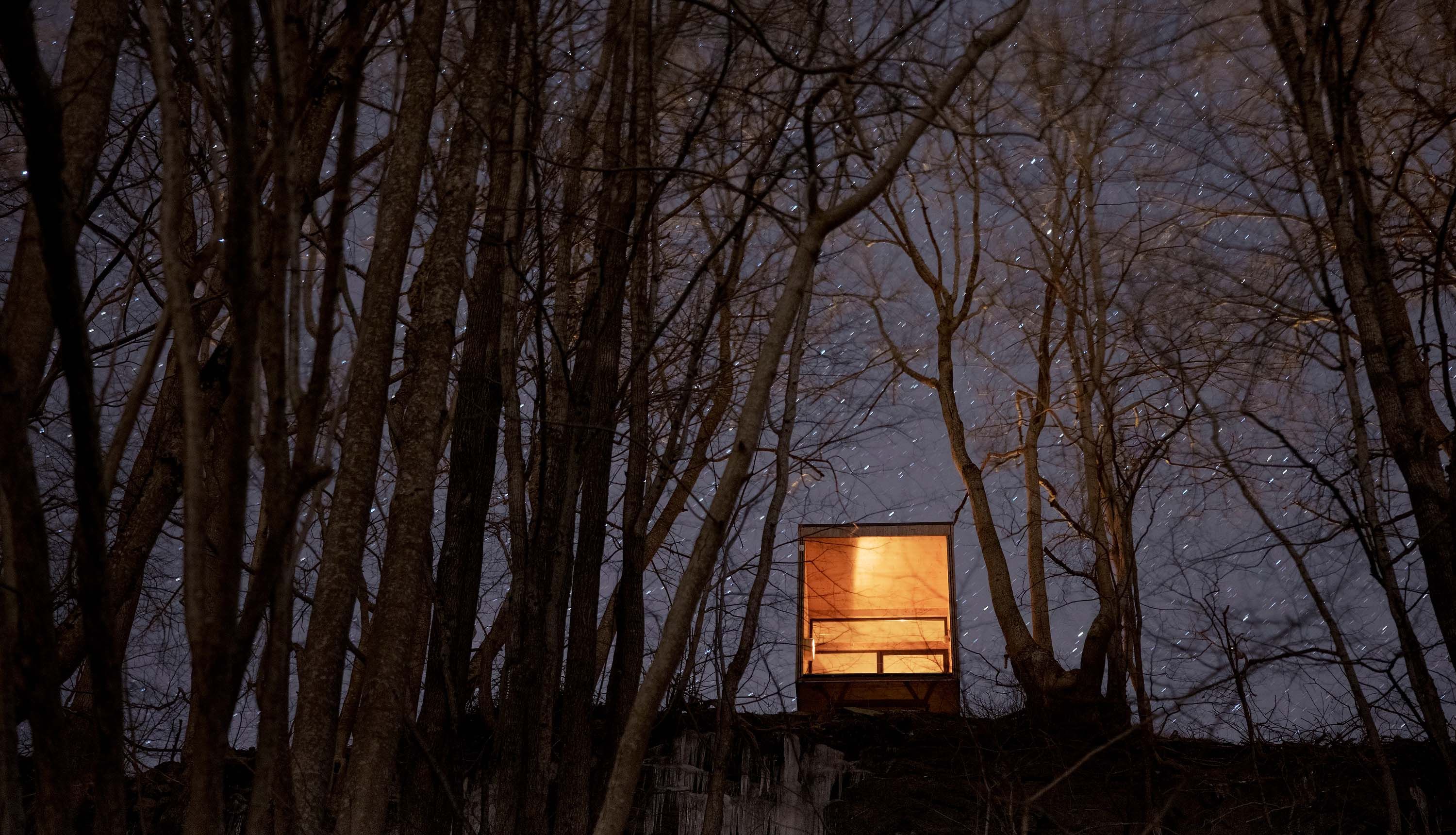 Cabin viewed from the forest, glowing in the night near Hardangerfjord.