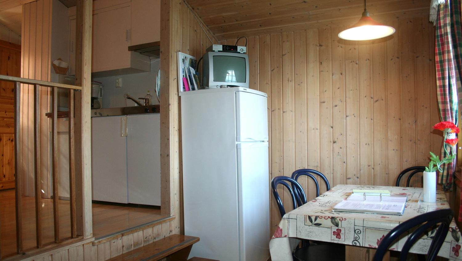 Klassisk hyttekjøkken med spisebord og TV i ei eldre hytte på Oddland Camping.