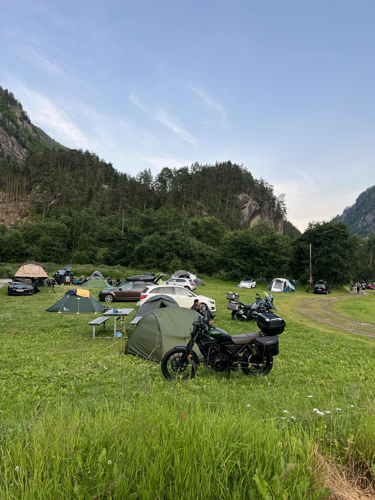 Motorsyklar og telt på Hildal Camping omgitt av grøne fjellsider og sommarkveld.
