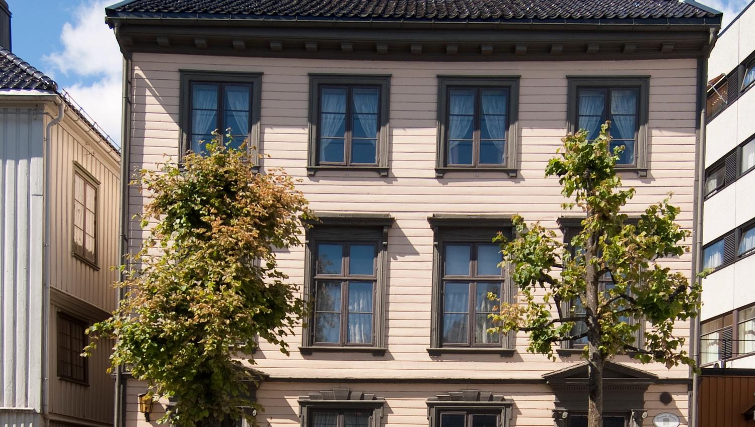 Frontfasade av Kløckers Hus, Arendal Bymuseum fra 1826. trehus i tre etasjer, beige liggende panel med militærgrønne vinduskarmer.