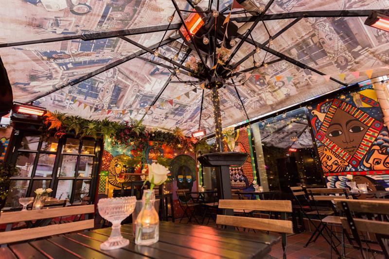 Outdoor seating, table and chairs under a parasol. A glass and a vase with a flower on the table.