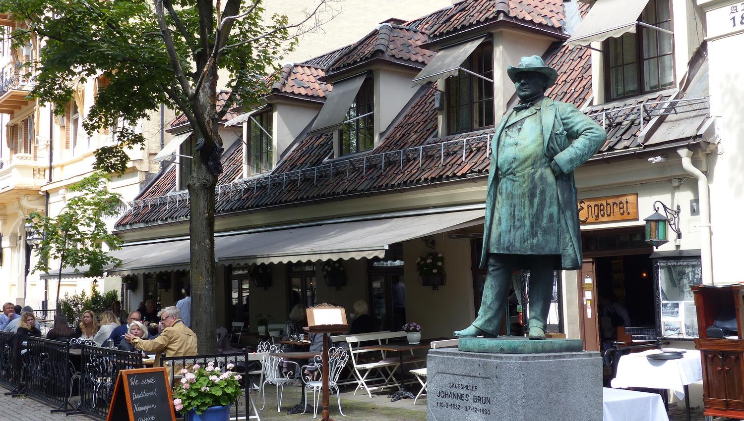 Eksteriør med uteservering ved siden av en statue.