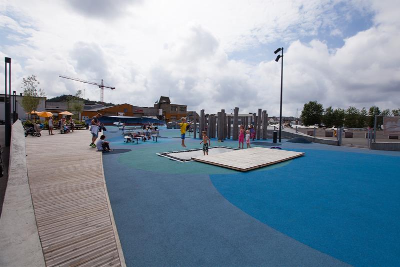 Buen Playground, blue in different shades on the ground with many different play equipment. Trampoline, swing, climbing wall, balance line