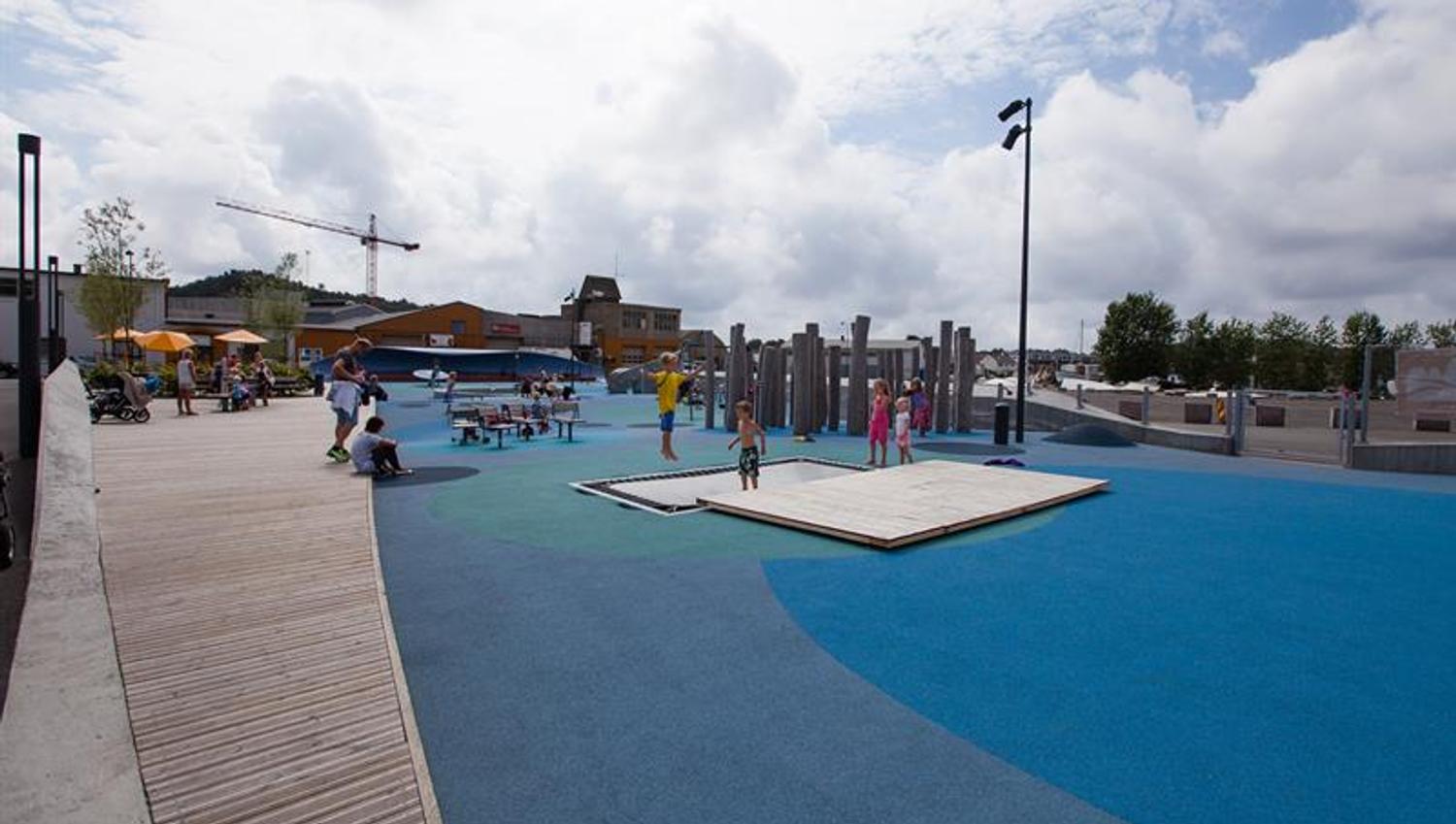 Buen Playground, blue in different shades on the ground with many different play equipment. Trampoline, swing, climbing wall, balance line