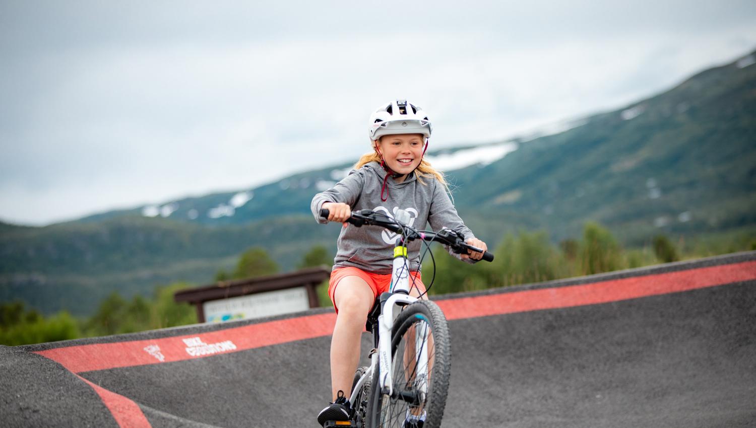 Ei smilende jente på sykkel på pumptracken i Vestlia Sykkelpark på Geilo.