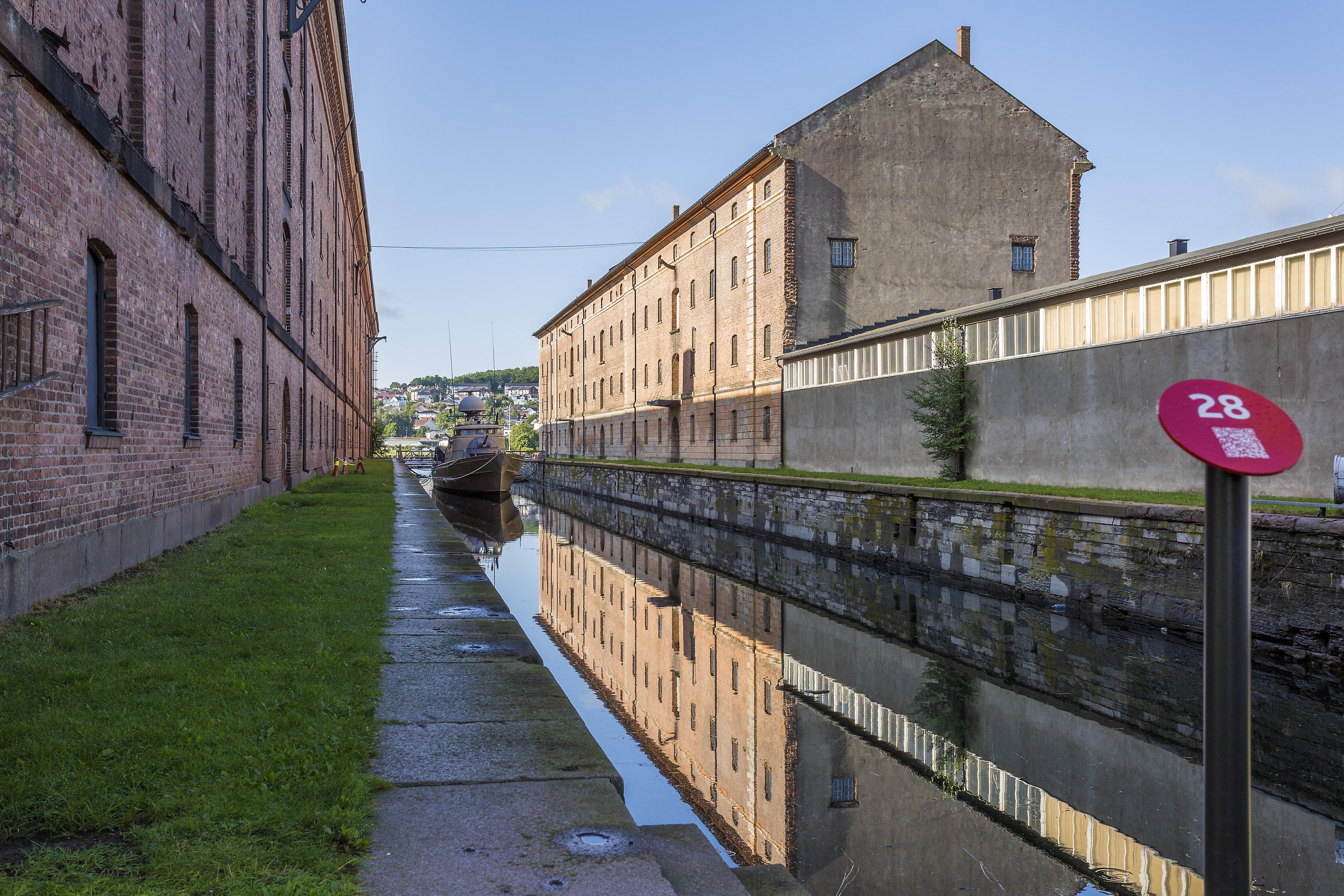 A long canal with water, brick buildings on either side and a boat lies at the bottom of the canal.