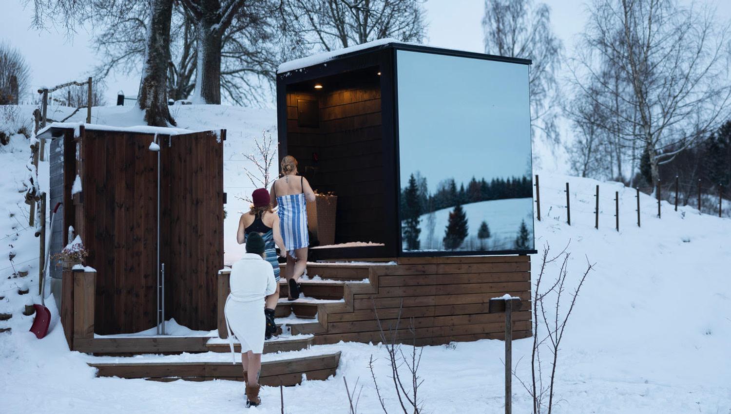 Jenter som går inn i en speilglassbadstue med snø utenfor