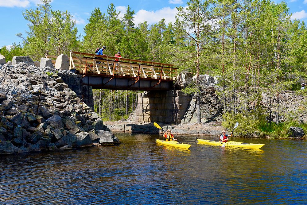 2 syklister ser ned på 2 kajakker som padler på elva