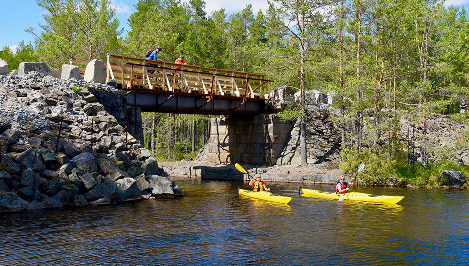 2 syklister ser ned på 2 kajakker som padler på elva