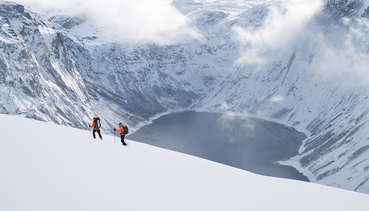 To trugevandrere i bratt vinterterreng med utsikt over fjorden ved Trolltunga.
