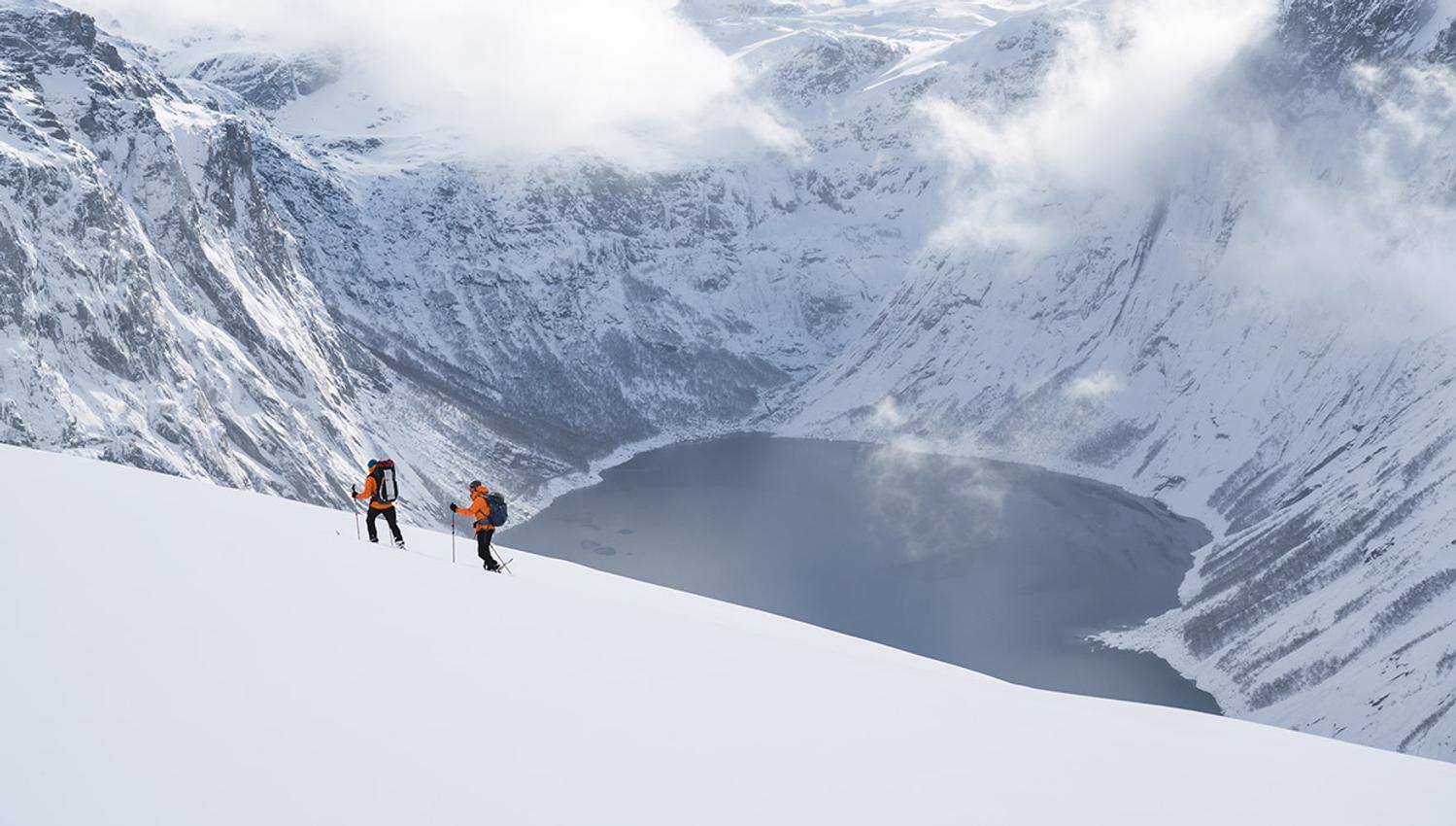 To trugevandrere i bratt vinterterreng med utsikt over fjorden ved Trolltunga.