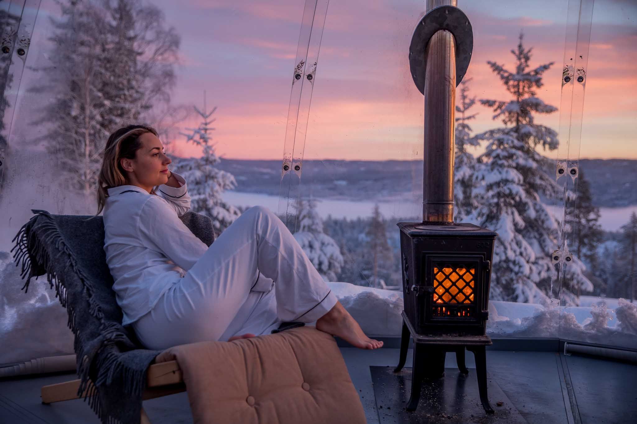 Jente som sitter ved en vedovn inne i igloen