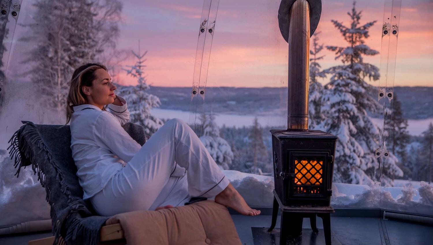 Jente som sitter ved en vedovn inne i igloen