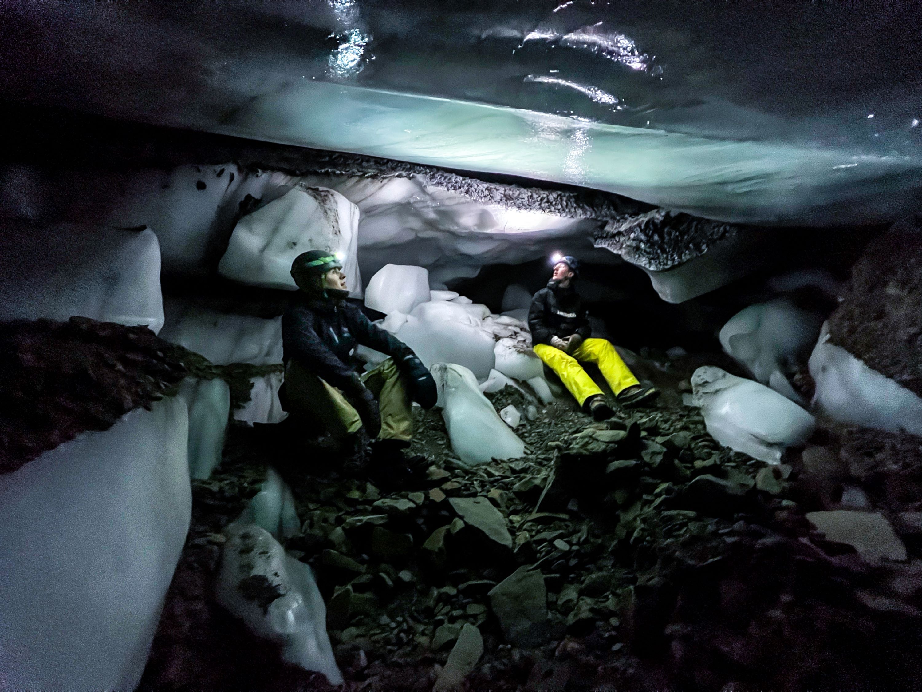 To people sitting on the ground inside an ice cave with head lamps on