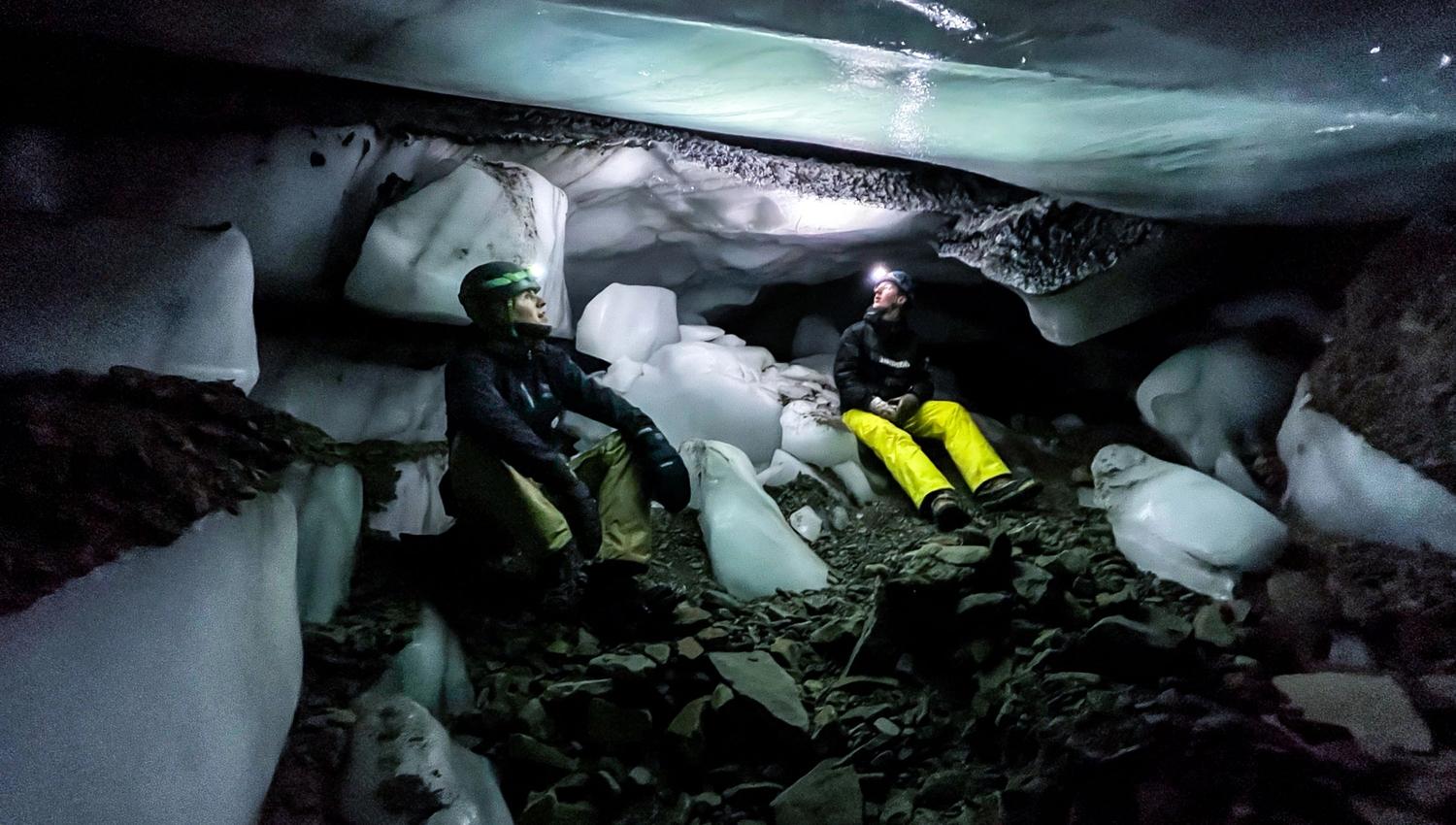 To people sitting on the ground inside an ice cave with head lamps on
