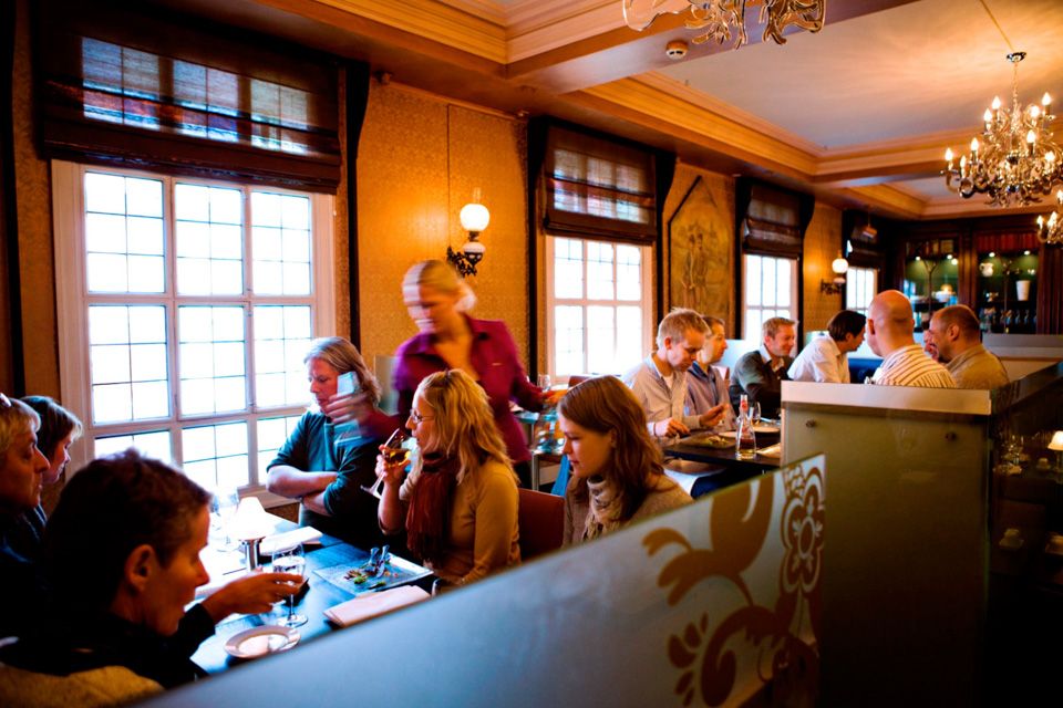 Diverse bord med sittende personer som spiser og drikker.