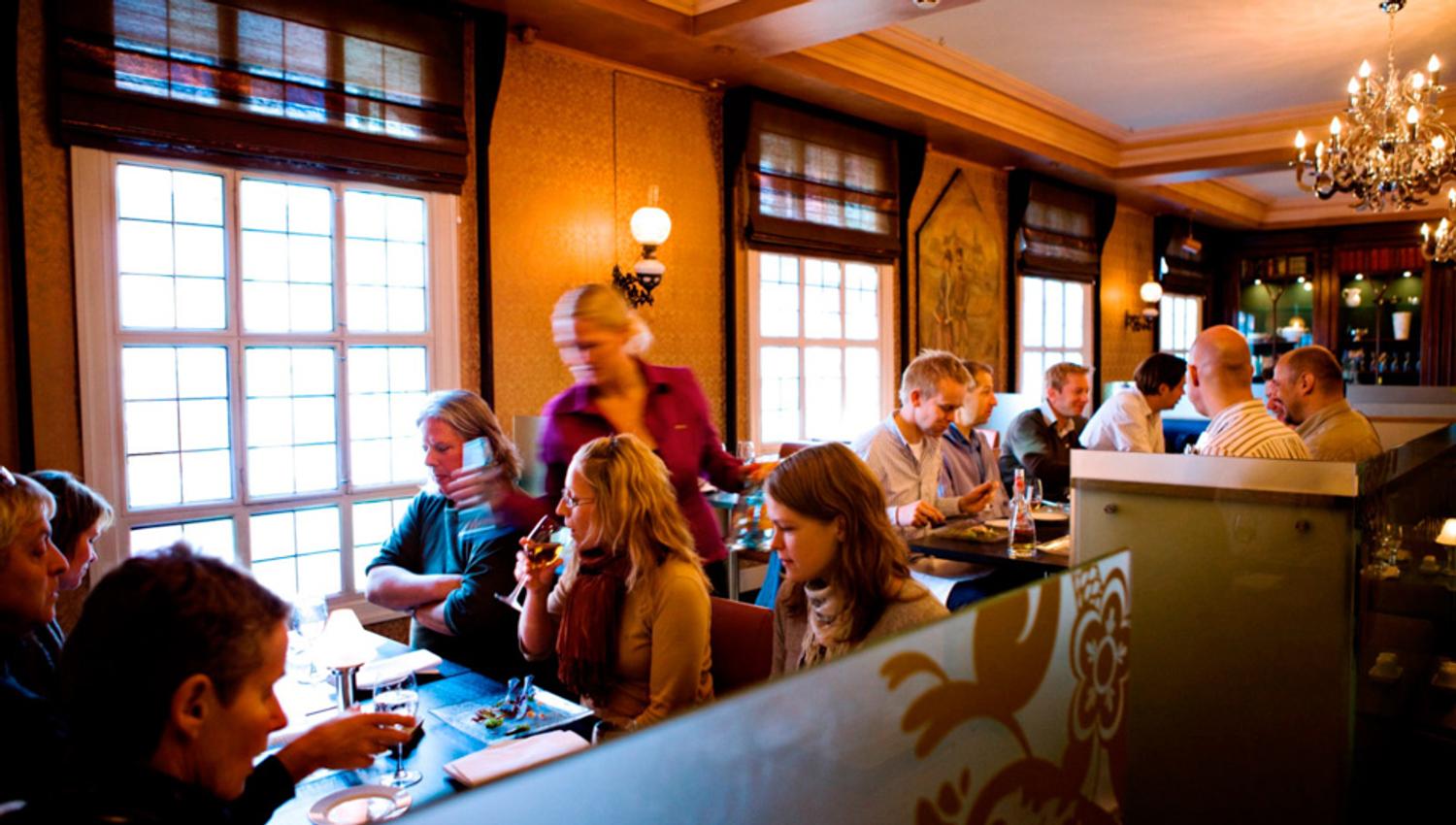 Diverse bord med sittende personer som spiser og drikker.