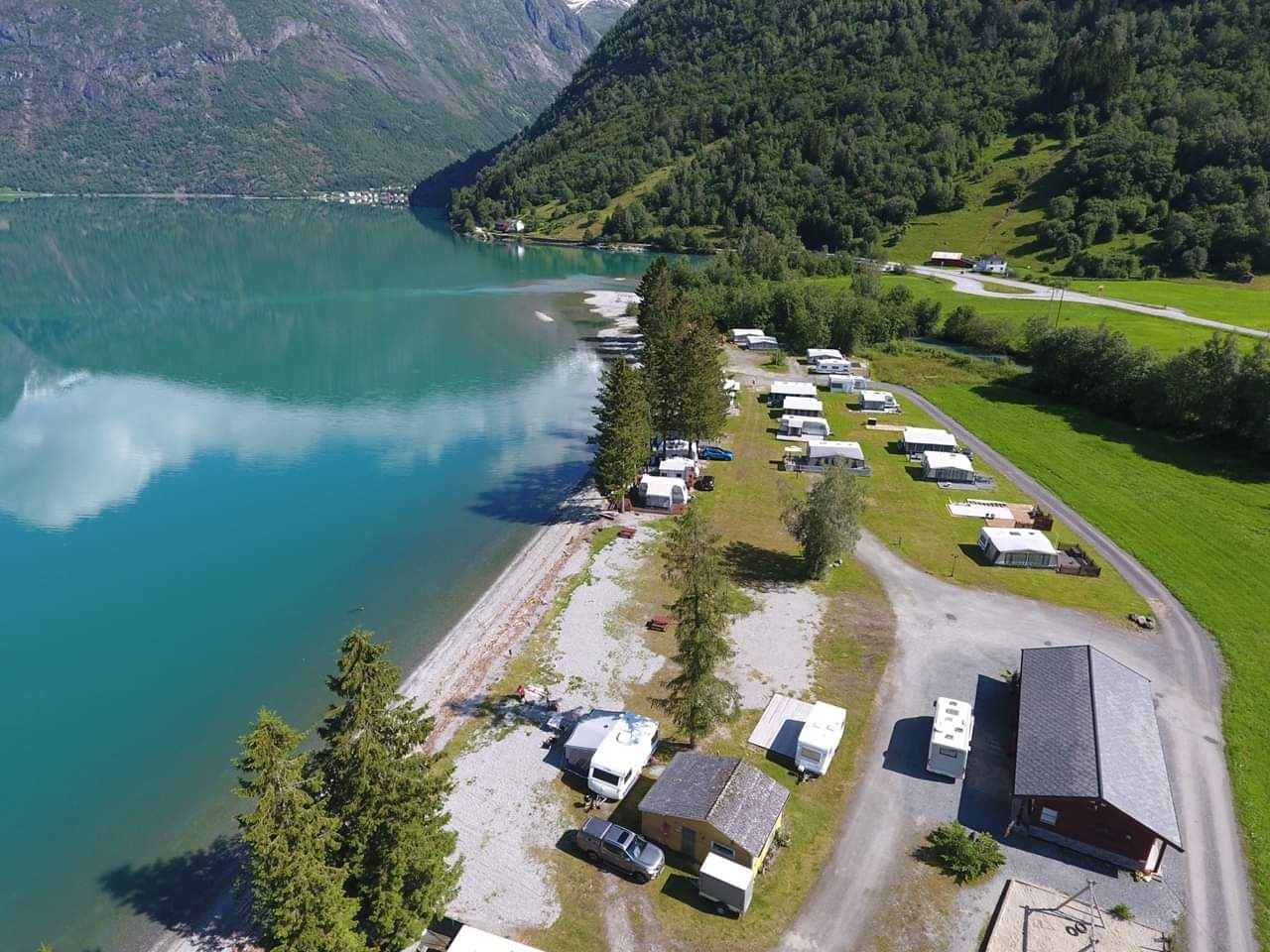 Droneutsikt over Grande Camping ved Oppstrynsvatnet i Oppstryn, omgitt av fjell og den blågrøne fargen frå brevatnet.