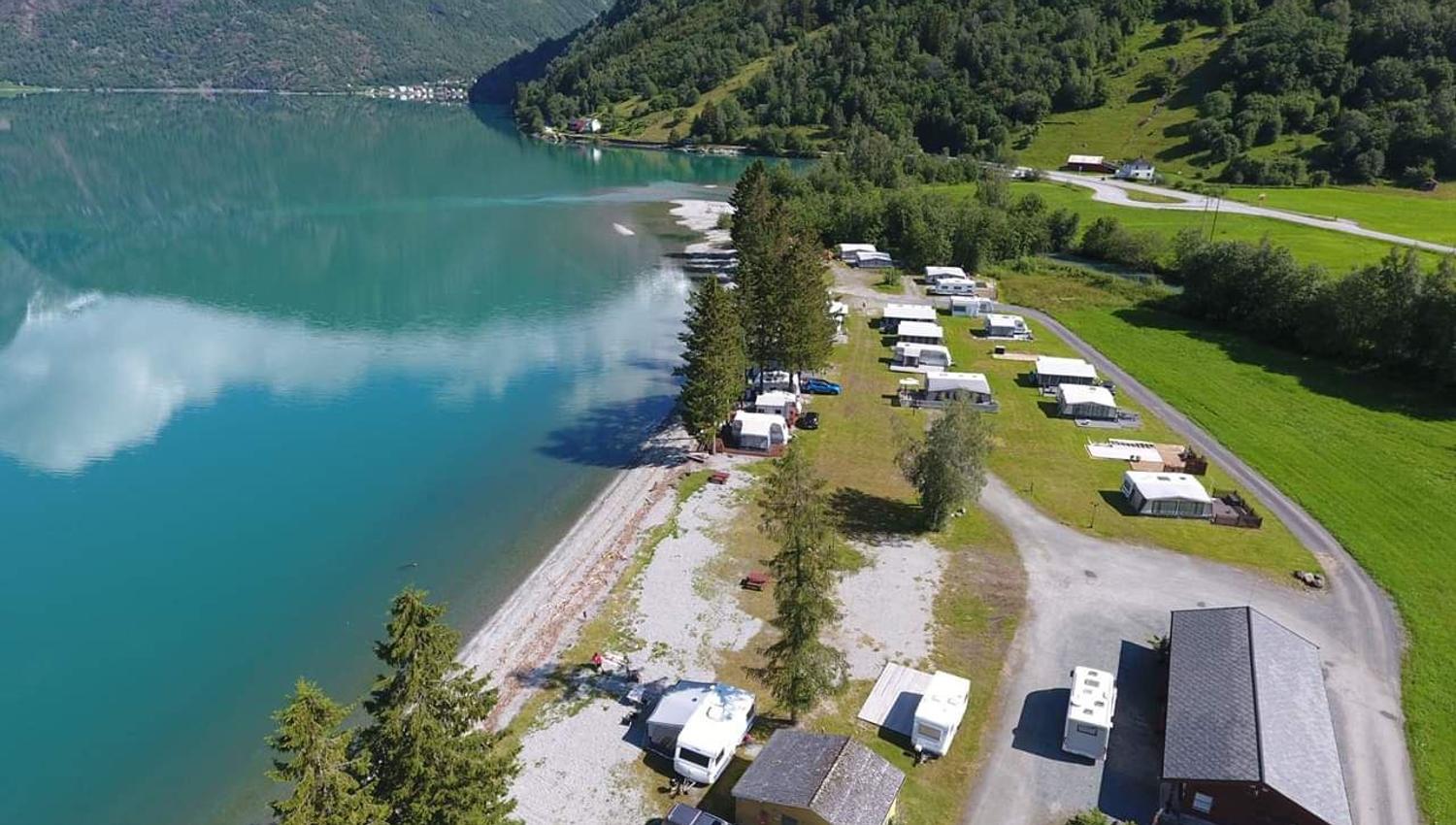 Droneutsikt over Grande Camping ved Oppstrynsvatnet i Oppstryn, omgitt av fjell og den blågrøne fargen frå brevatnet.