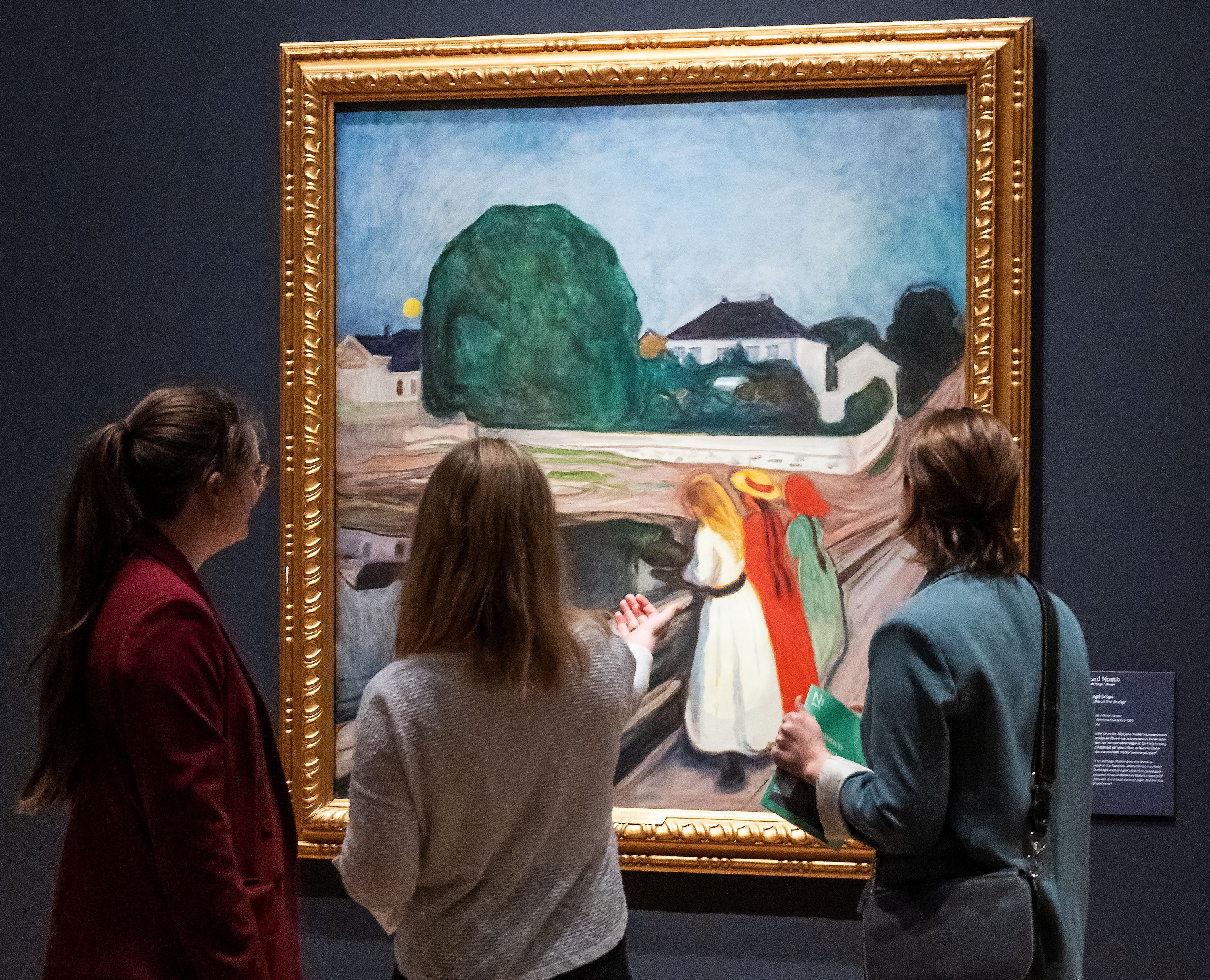 Tre jenter som ser på maleriet "Pikene på boren" av Edvard Munch.