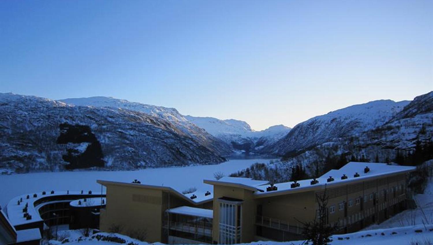 Vinterutsikt over Hordatun Hotel og Røldalsvatnet, omgitt av mektige fjell og eit snødekka landskap.