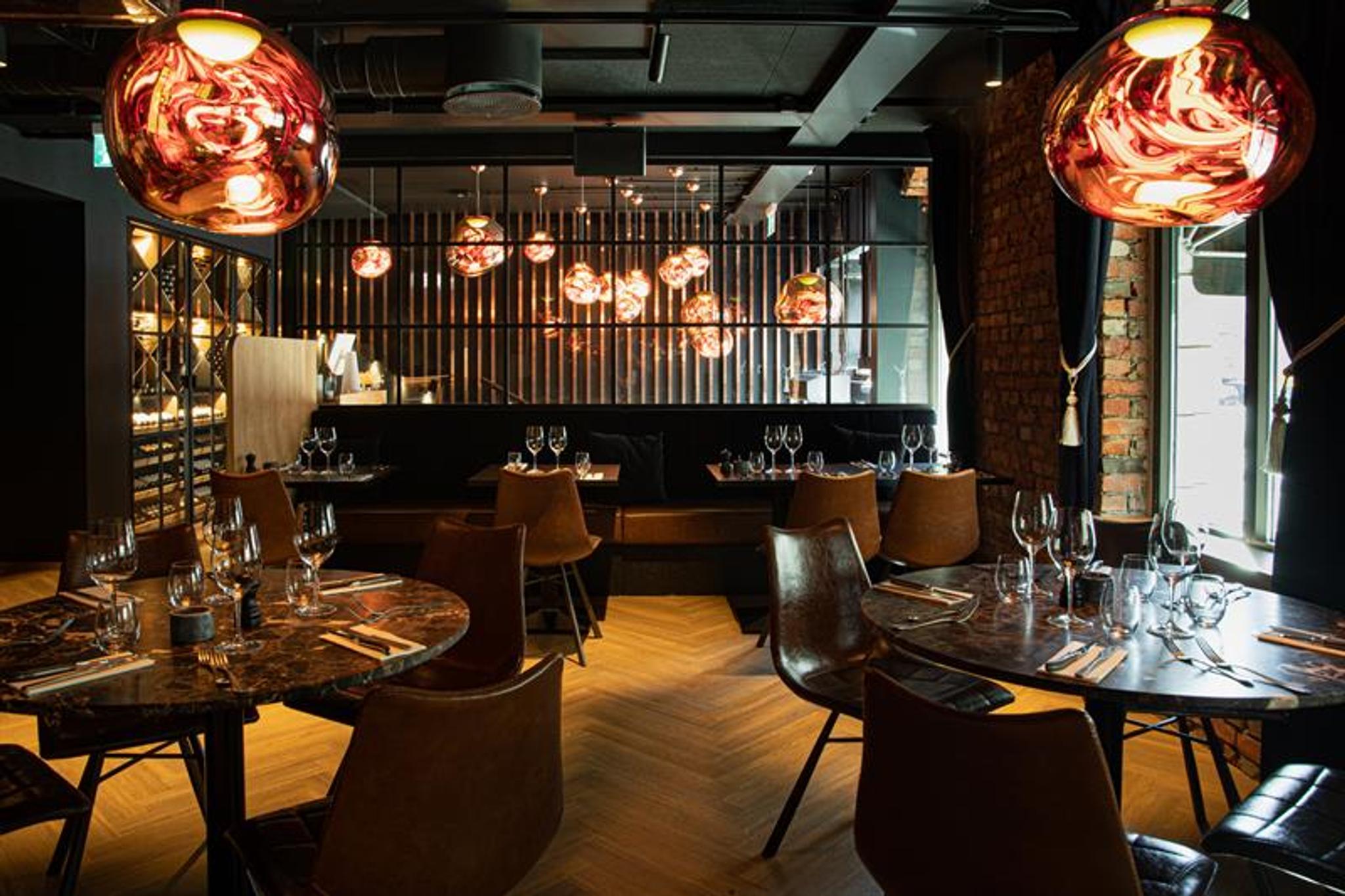 Restaurantinteriør med runde, brune bord, brune stoler og sitteseksjon mot veggen.