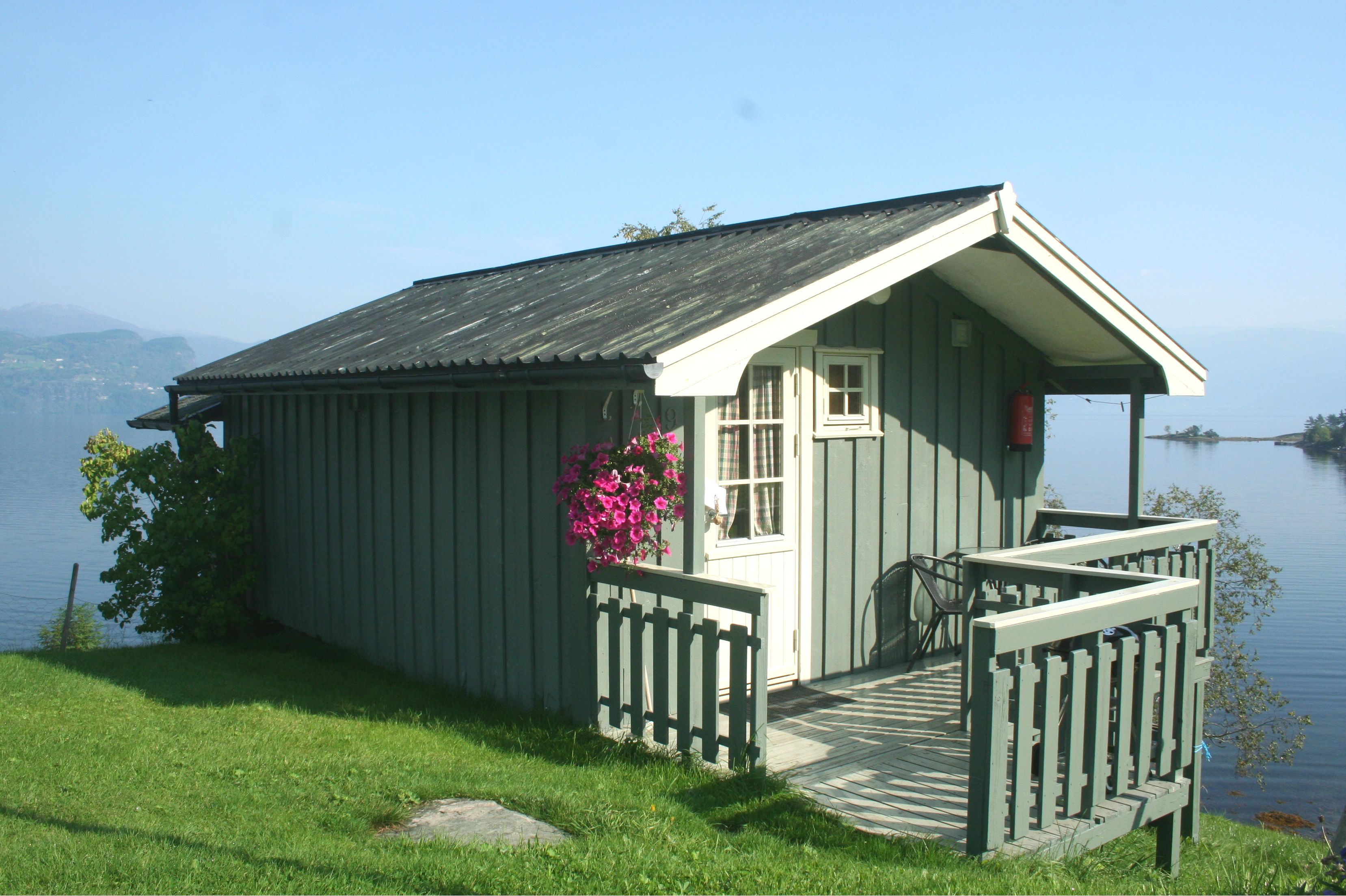 Lita hytte med blomstrande hengplante og utsikt over fjorden frå Oddland Camping.