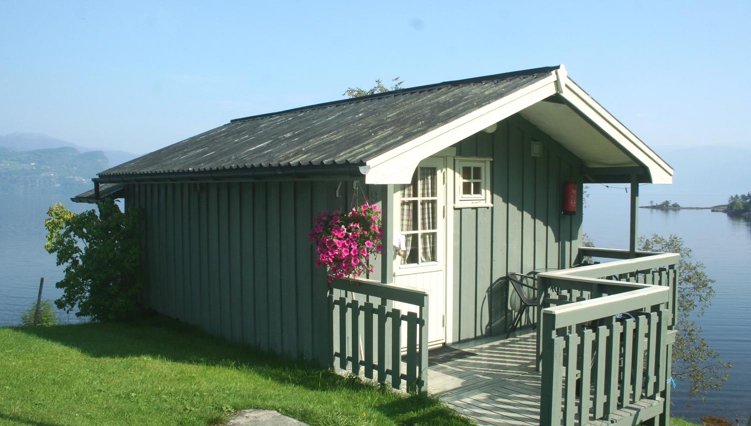 Lita hytte med blomstrande hengplante og utsikt over fjorden frå Oddland Camping.