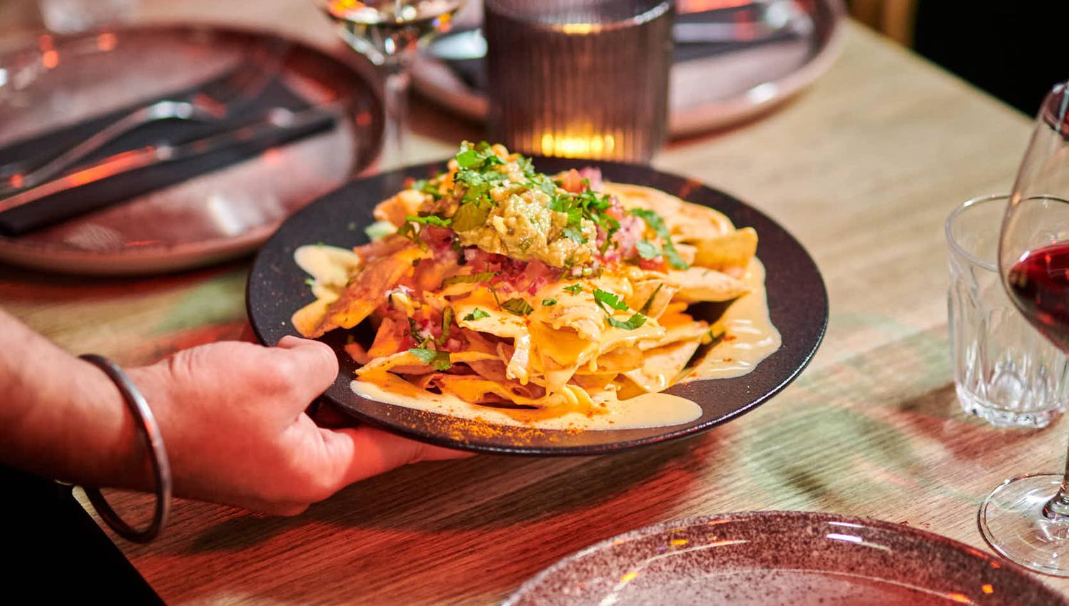 En tallerken med nachos blir servert ved et bord dekket med glass og bestikk.