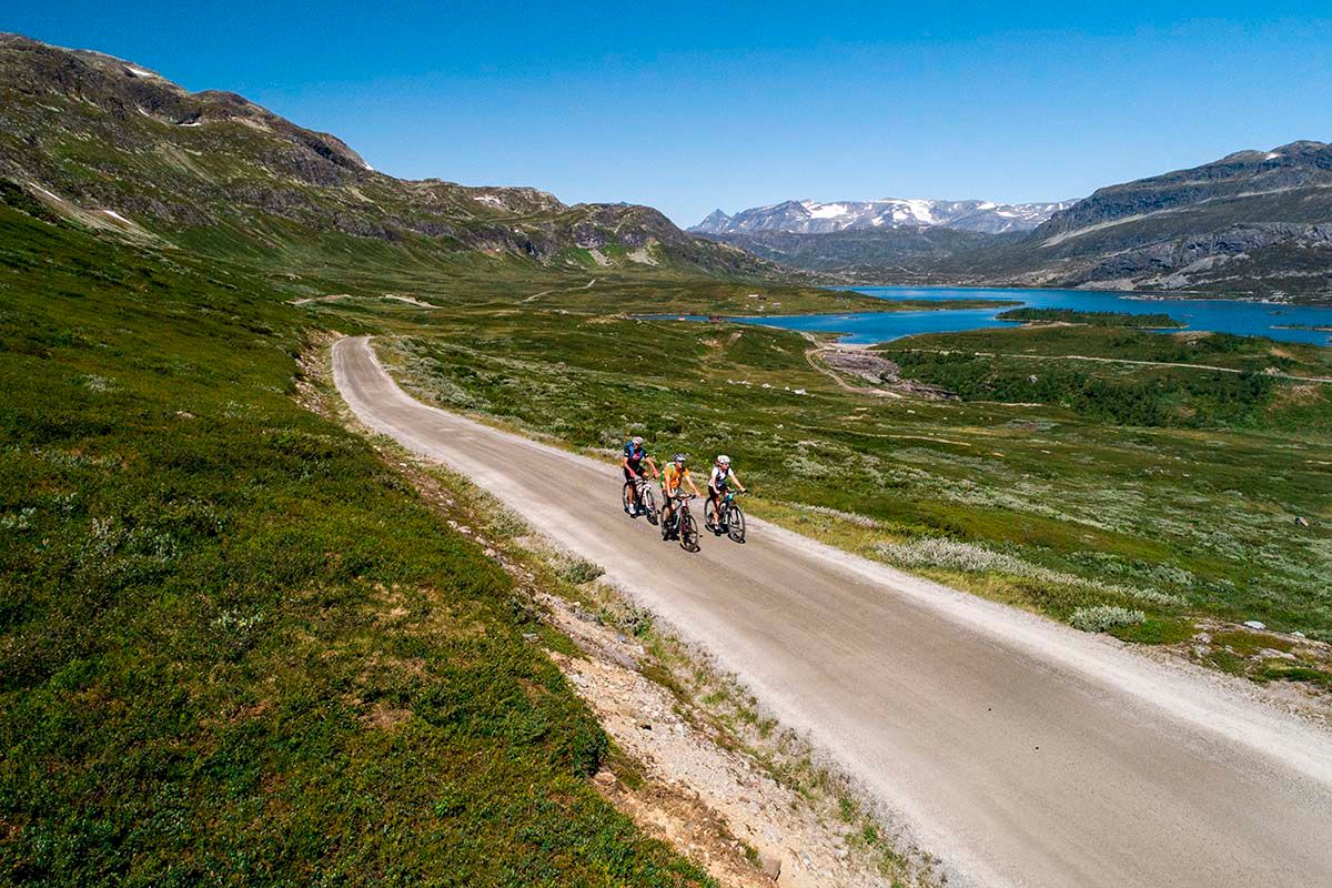 Cyclists on the climb on a gravel road to a mountain pass, with Jotunheimens high peaks in the background.