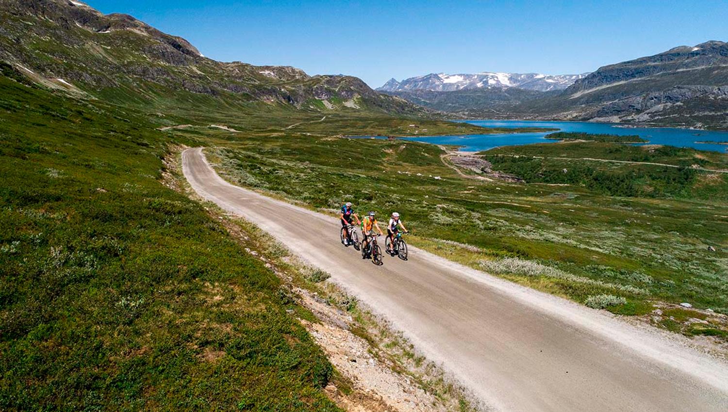Cyclists on the climb on a gravel road to a mountain pass, with Jotunheimens high peaks in the background.