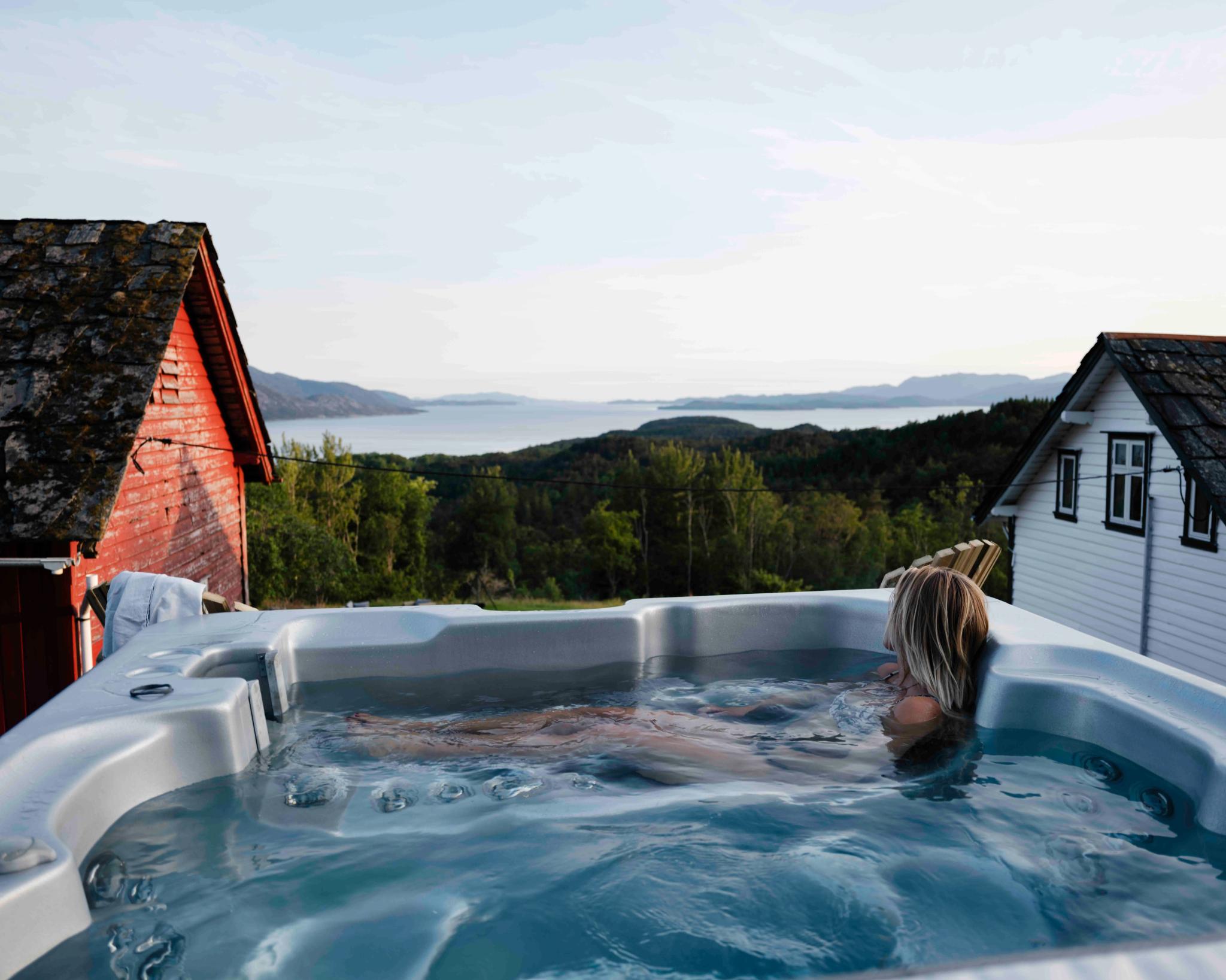 Relaxing in an outdoor hot tub with panoramic Hardangerfjord views at Stigen Fjordlodge.