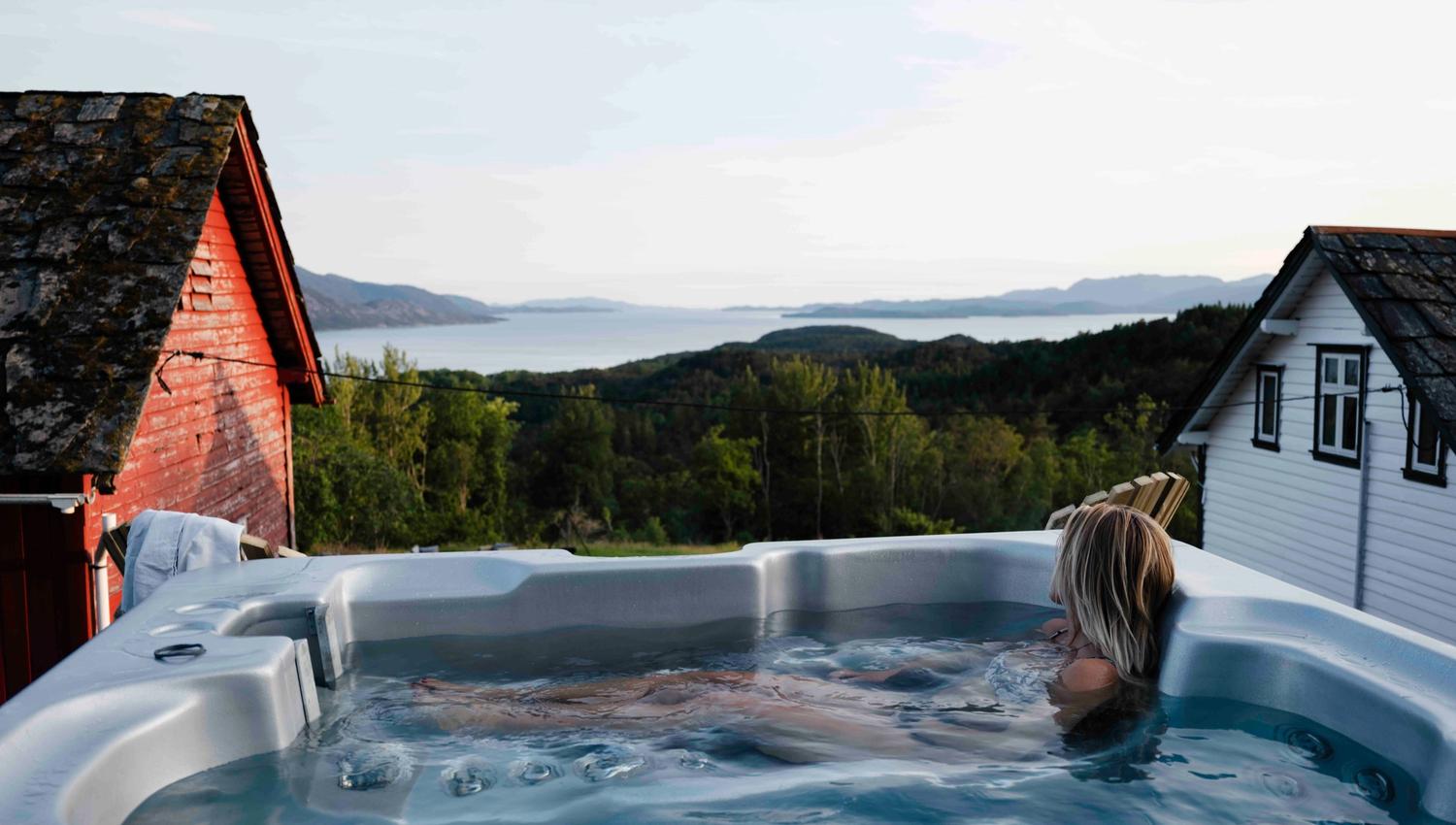 Person slappar av i utespa med panoramautsikt over Hardangerfjorden på Stigen Fjordlodge.