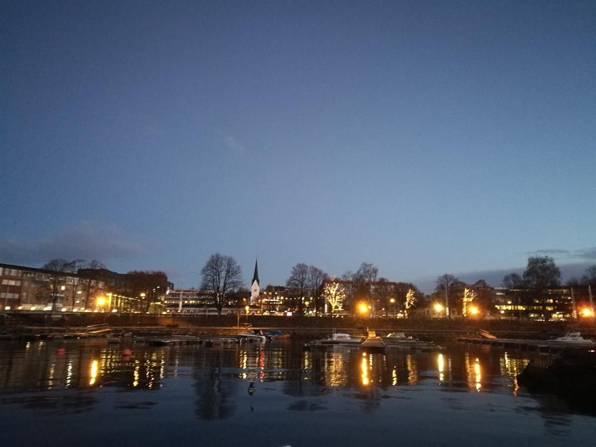 Båthavna i Hamar, Kveldsutsikt over en by ved vannet, med bygninger som speiler seg i overflaten.