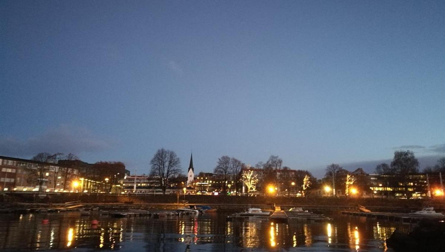 Båthavna i Hamar, Kveldsutsikt over en by ved vannet, med bygninger som speiler seg i overflaten.