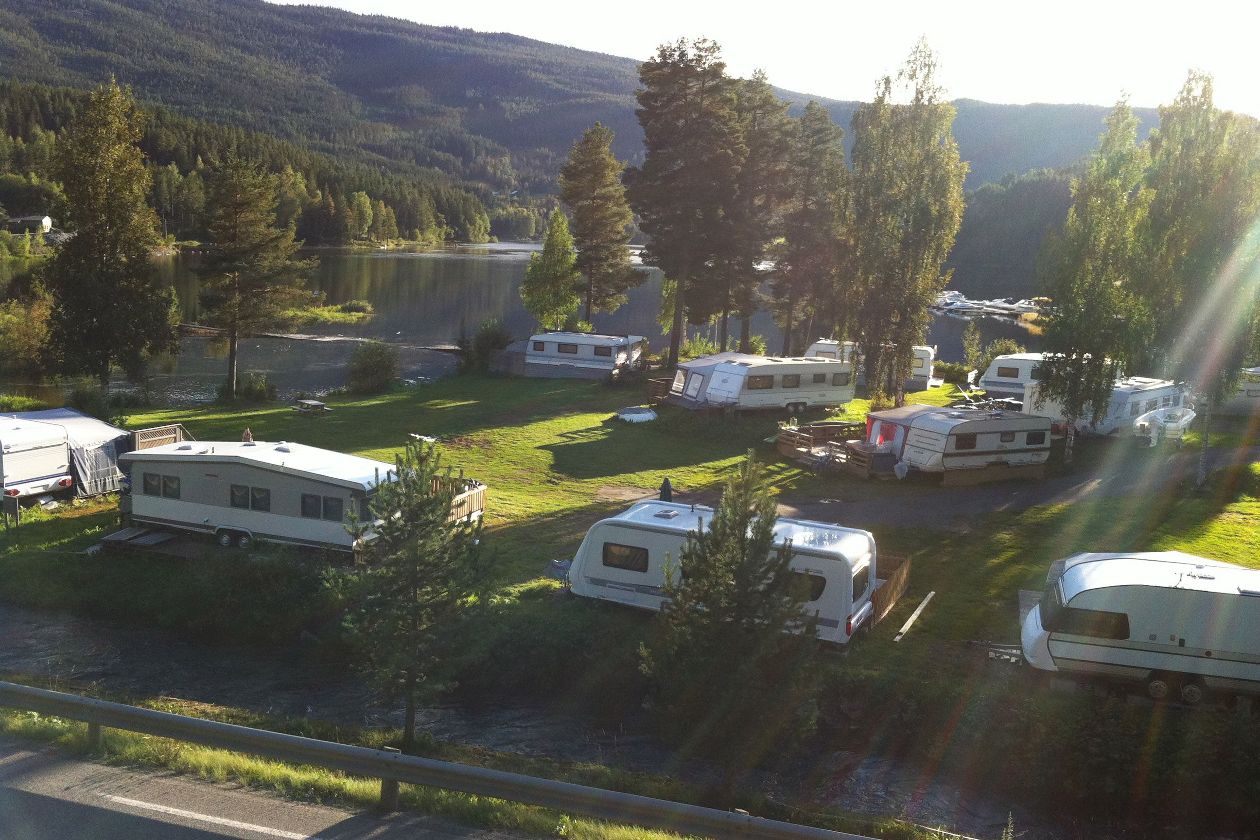 A campground by a lake during summer with caravans on a green lawn.